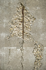 Damaged concrete surface on which cracks and blistered areas reveal a rusty reinforcement bar