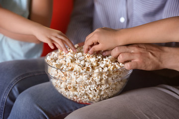 Family eating popcorn while watching TV in evening, closeup
