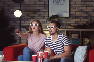 Young couple in 3d glasses watching movie on sofa at night