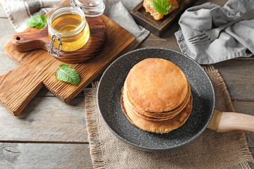 Frying pan with tasty pancakes and honey on wooden table