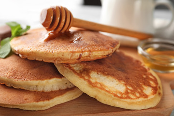 Board with tasty pancakes and honey on table, closeup