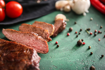Tasty cut grilled meat with fresh spices on green table, closeup