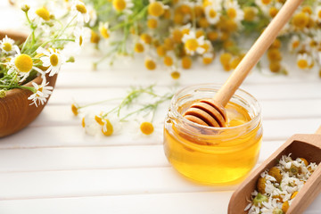 Jar of honey with chamomile flowers on wooden table