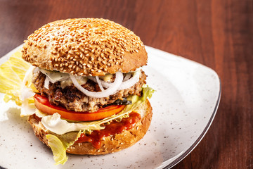 American burger with homemade bun with sesame seeds, fried meat kettle, tomatoes, lettuce and fresh onions. Copy space