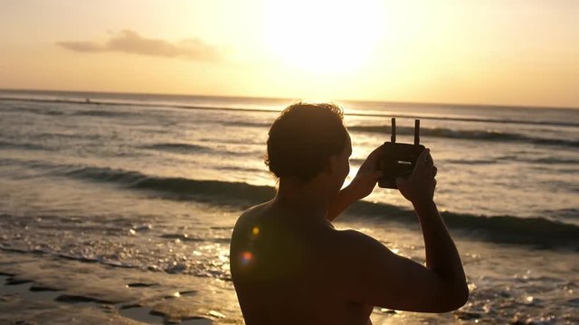 Man operating a drone with remote control. Quadro copter drone flying over sunset ocean. 3840x2160
