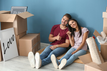 Young happy couple with key and moving boxes sitting on floor at new home