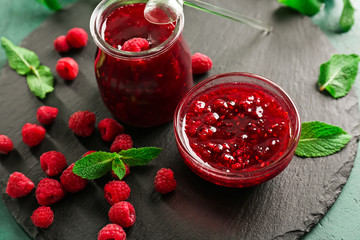 Slate plate with glass jar and bowl of tasty raspberry jam on green table