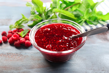 Bowl with tasty raspberry jam on wooden table