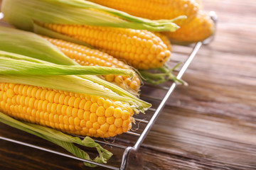 Cooling rack with tasty corncobs on wooden table, closeup