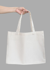 Tote bag canvas white cotton fabric cloth eco shopping sack mockup blank template isolated on grey background (clipping path) with woman’s handling hand