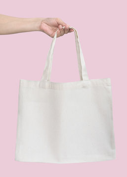 Tote bag canvas white cotton fabric cloth for eco shoulder shopping sack mockup blank template isolated on pastel pink background (clipping path) with woman’s handling hand