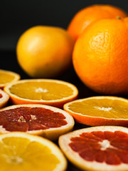 Fototapeta na wymiar Citrus still life on dark background. Sliced and whole oranges and grapefruits.