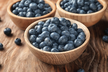Bowls with ripe blueberries on wooden table, closeup