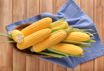 Basket with tasty corncobs on wooden table