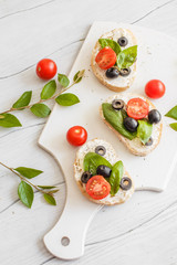Sandwiches with cream cheese tomatoes, olives and basil on a wooden white board