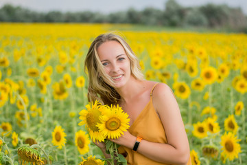 Naklejka na ściany i meble Happy woman with sunflowers. The girl in the fields of a sunflower