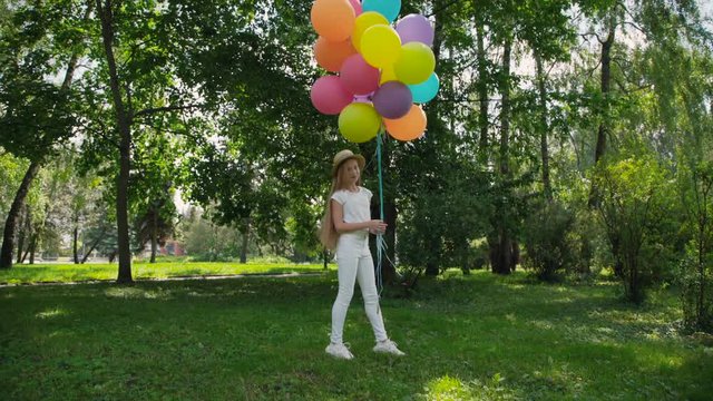 Happy young girl poses in the green sunny park and holds colourful balloons