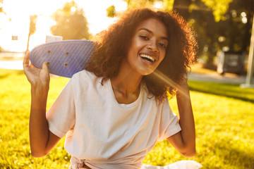 Delighted young african girl holding skateboard