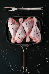flat lay with raw turkey legs with pepper corns and salt in grill pan with meat fork on black