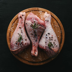 top view of raw turkey legs with pepper corns and rosemary on wooden cutting board