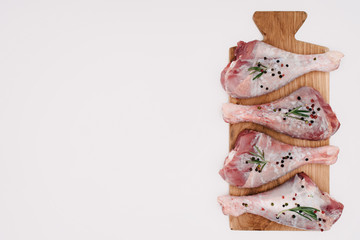 top view of chicken legs with pepper corns, rosemary and salt on cutting board, isolated on white