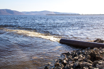 Dirty water flows out of a large metal rusty pipe under pressure into the river.