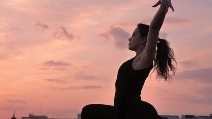 Yogi girl is changing poses from one legged downward-facing dog to warrior one on rooftop in summer...
