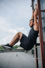 side view of handsome sportsman working out on ladder on roof