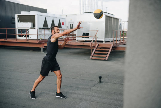 handsome sportsman catching medicine ball on roof