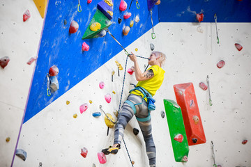 Photo from back of young ahtlete girl in sportswear scrambles on wall for climbing at workout