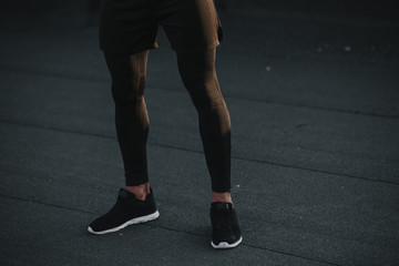 cropped image of sportsman standing in black sneakers and leggings on roof - obrazy, fototapety, plakaty