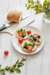 Sandwiches with cream cheese tomatoes, olives and basil on a wooden white board