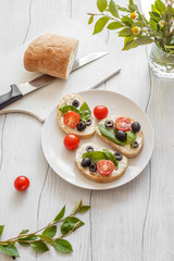 Fototapeta na wymiar Sandwiches with cream cheese tomatoes, olives and basil on a wooden white board