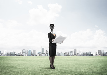 Camera headed woman standing on green grass against modern citys