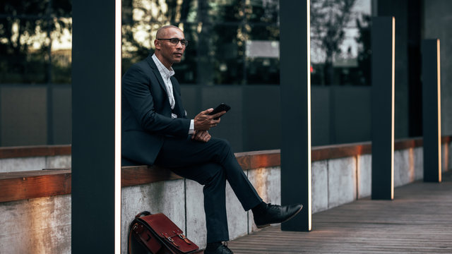 Businessman sitting outdoors holding his mobile phone