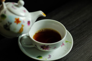 Tea or coffee set: pot and cup, dark background, selective focus