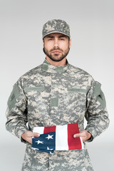 portrait of male soldier in military uniform with american flag in hands on grey backdrop