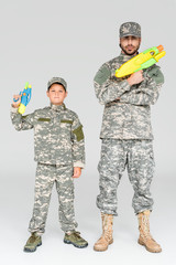 father and son in military uniforms with toy water guns on grey background