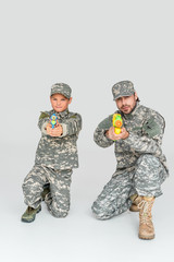 father and son in military uniforms with toy water guns on grey background
