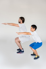 side view of boy and father squatting together on grey background