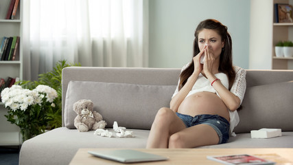 Sick pregnant woman blowing stuffy nose in tissue, feeling bad, cought cold