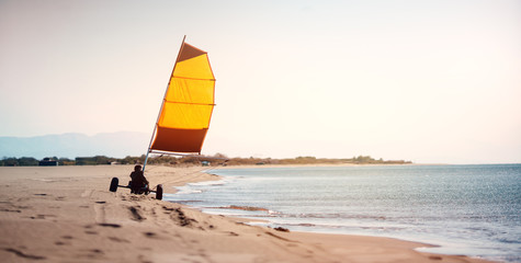 Man sails on the land in buggy near the sea during windy winter day; land sailing, sailing buggy.