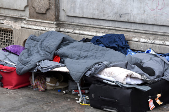 Auf einem Bürgersteig an einer Hauswand stehende Liege mit schlafendem Obdachlosen