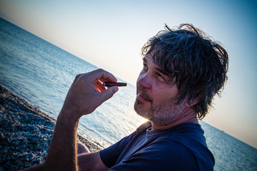 A man with a cigar looking at camera / Portrait of good looking middle aged man on the beach while...