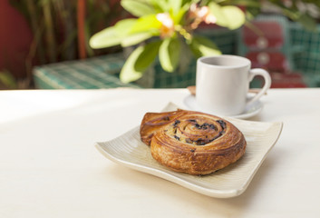 Homemade French spiral Chocolate danish with hot coffee on wooden table over blurred garden and pool background, morning outdoor day light, breakfast concept 