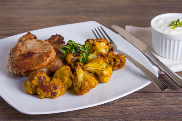 Delicious pork meat and fried cauliflowers as a side dish, served with tartar sauce on a wooden table. Close up.