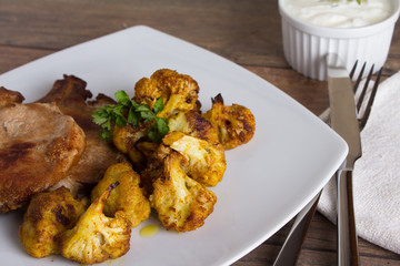 Delicious pork meat and fried cauliflowers as a side dish, served with tartar sauce on a wooden table. Close up.