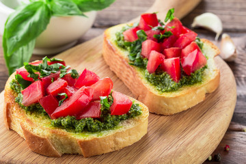 Bruschetta with fresh pesto, basil leaves and tomatoes. Wooden background