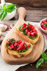 Bruschetta with fresh pesto, basil leaves and tomatoes. Wooden background