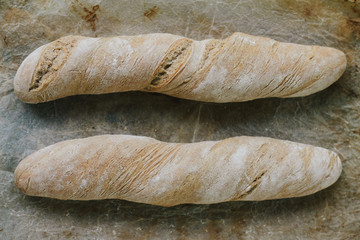 Two tasty, homemade loafs of bread on rustic tray covered with flour on the crust.